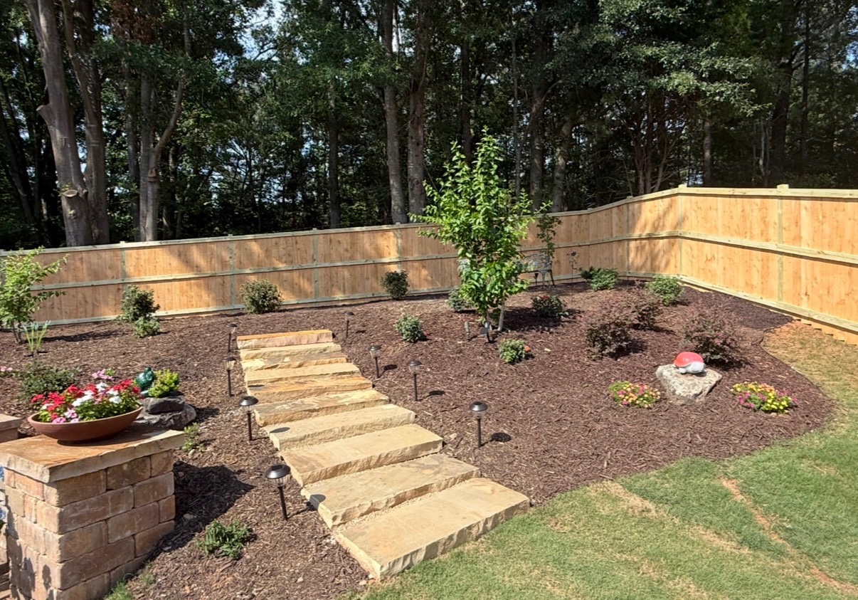 Natural stone steps climbing a mulched slope with plantings, path lights and a low stone wall